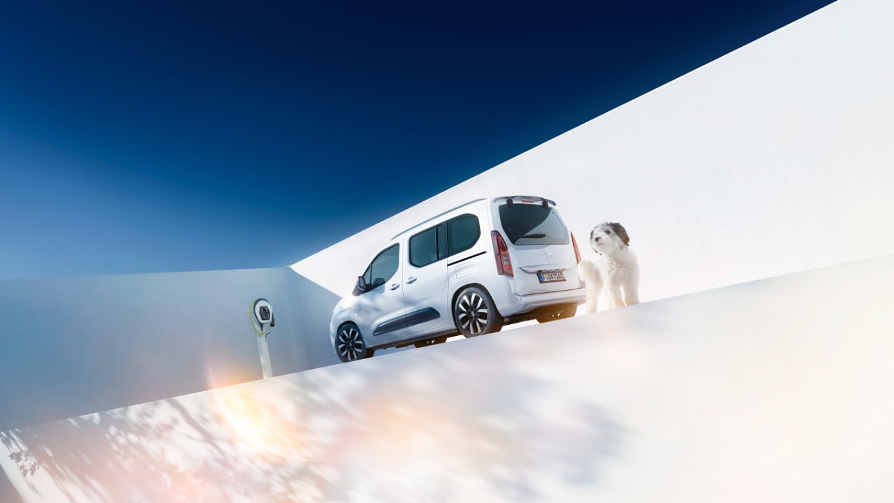 Bočný pohľad zozadu na biely Opel Combo Electric so psom vedľa nástennej nabíjačky